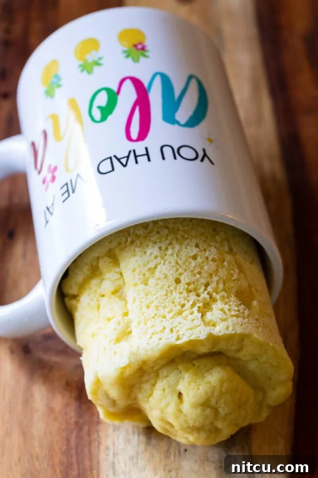 Effortless Keto Mug Bread 2 White mug on its side with a loaf of bread half hanging out.