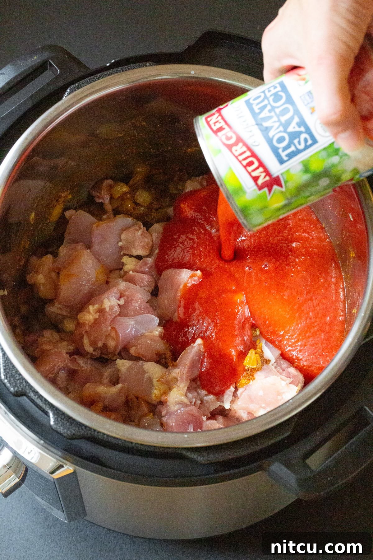 Raw chicken and tomato sauce being poured into instant Pot. 