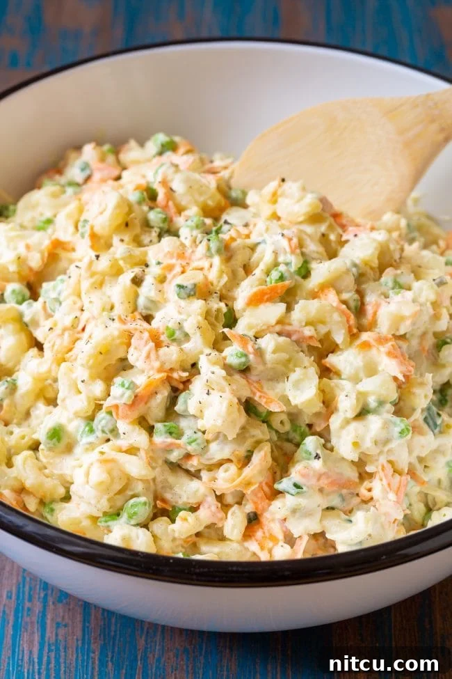 Creamy Hawaiian Macaroni Potato Salad 2 Bowl of potato and mac salad with a wooden spoon, showcasing the creamy texture and vibrant ingredients.