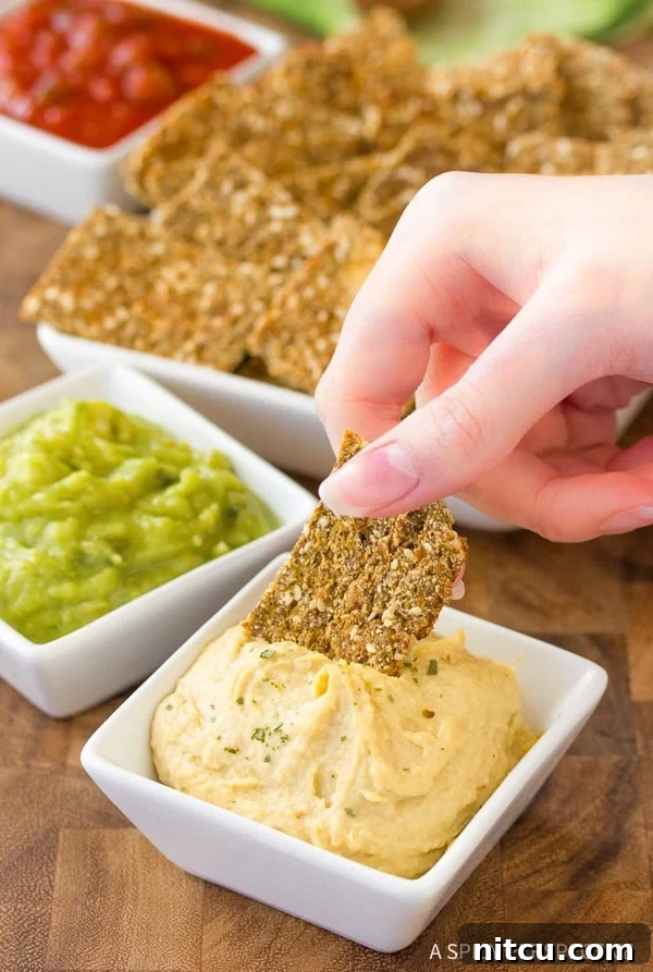 Crispy Keto Cauliflower Bites 3 A hand dipping a golden cauliflower cracker into a small white bowl of creamy hummus, highlighting its perfect crunch and versatility.