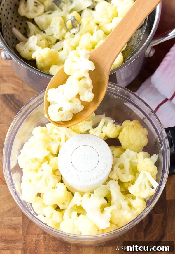 Crispy Keto Cauliflower Bites 5 A wooden spoon carefully adding steamed and cooled cauliflower florets into a food processor for mincing.