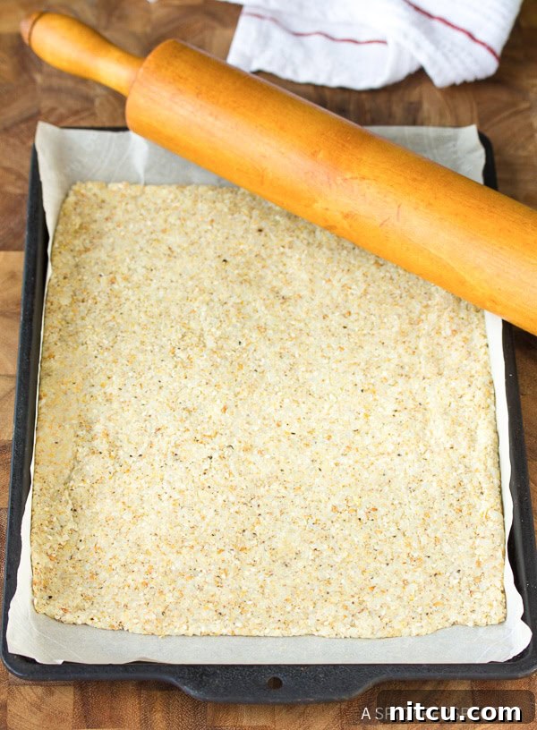 Crispy Keto Cauliflower Bites 7 A baking sheet covered with a thin, evenly rolled layer of raw cauliflower cracker dough, ready for its first bake.