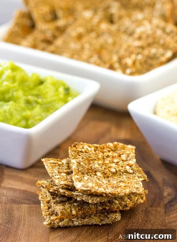 Crispy Keto Cauliflower Bites 9 A vibrant stack of low carb cauliflower crackers arranged next to small white square dishes filled with various colorful dips, showcasing their perfect texture and serving versatility.