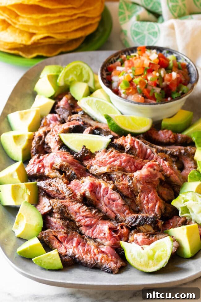 The Secret to Tender Carne Asada 2 Perfectly seared Carne Asada steak, garnished with fresh avocado and lime wedges, ready to be enjoyed.