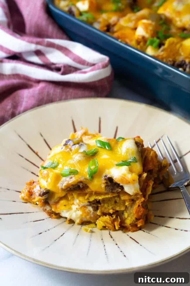 A generous slice of Cool Ranch Dorito Casserole on a plate, showcasing its vibrant layers of cheese, meat, and chips.