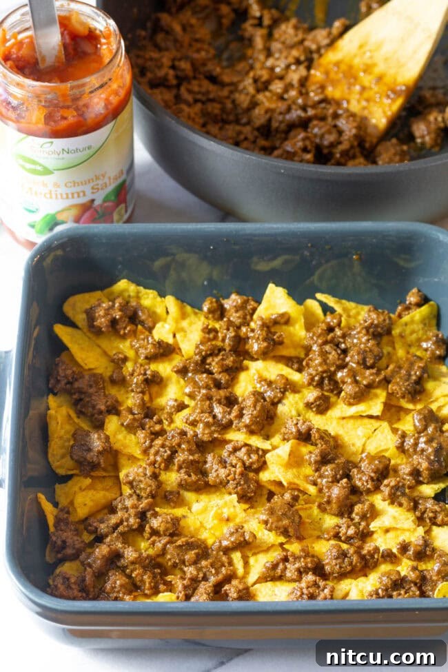 A layer of cooked minced meat spread over crushed Doritos in a baking dish.