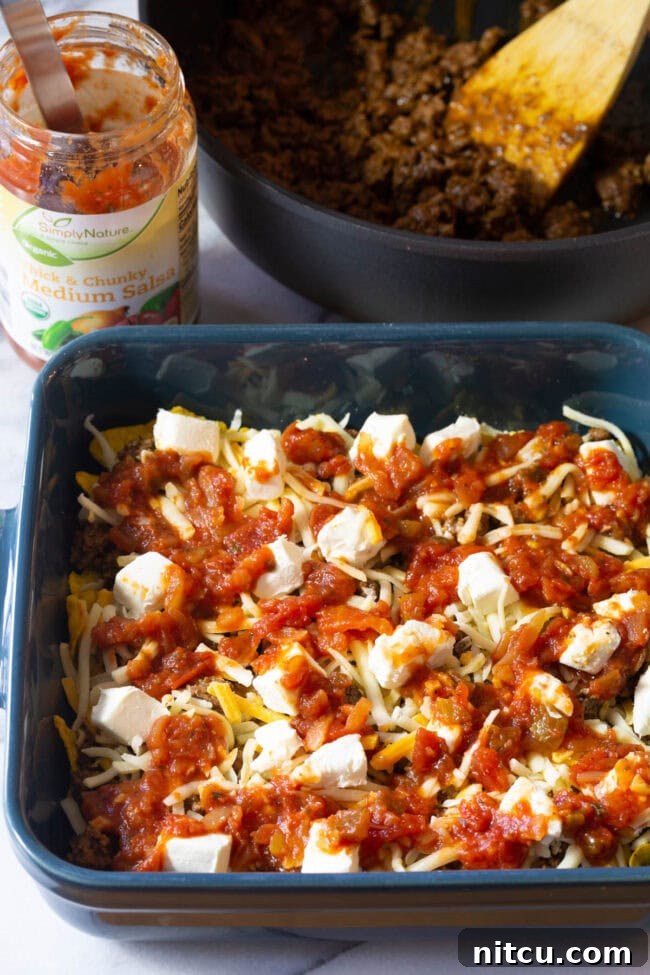 Dorito, meat, and cheese mixture covered with a vibrant layer of salsa in a baking dish.