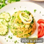 Thai fried rice recipe in a mound on a plate next to tomatoes, cucumbers and limes.