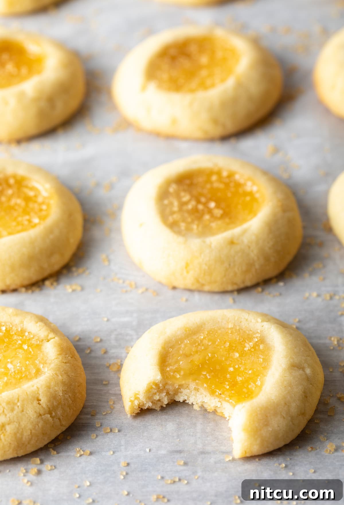 Sunshine Lemon Drop Cookies 8 One lemon thumbprint cookie has a bite taken out of it laying on the baking sheet with the others