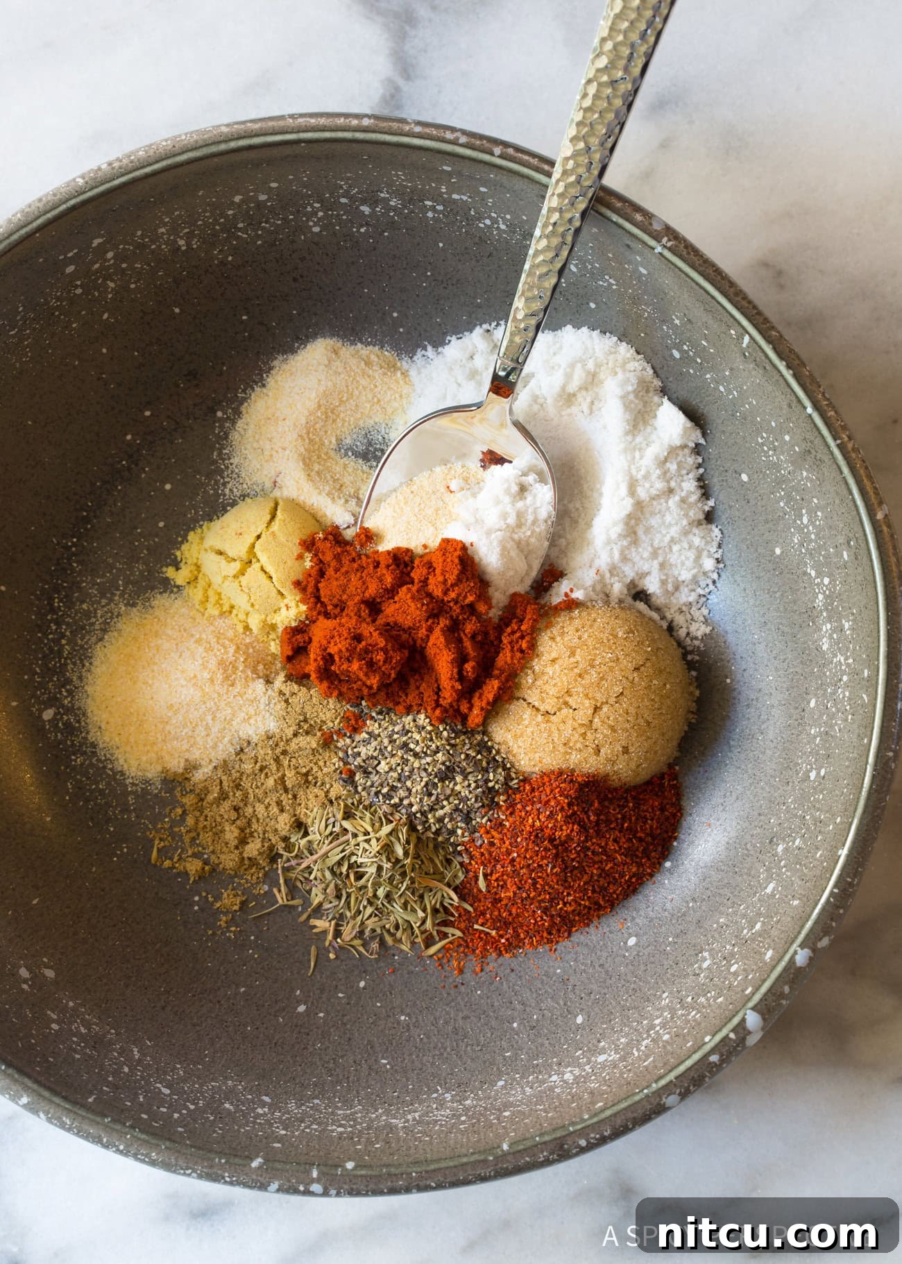 Herbs and Spices for the Best Steak Seasoning A small white bowl filled with a rich, vibrant blend of herbs and spices, showcasing the key ingredients for homemade steak seasoning.