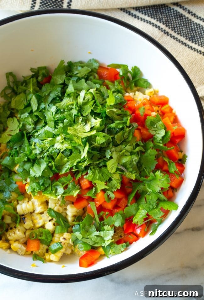 Charred Mexican Elote 8 Overhead view of a bowl brimming with fresh, vibrant ingredients for street corn salad: colorful cilantro, red bell pepper, grilled corn, and green onions.