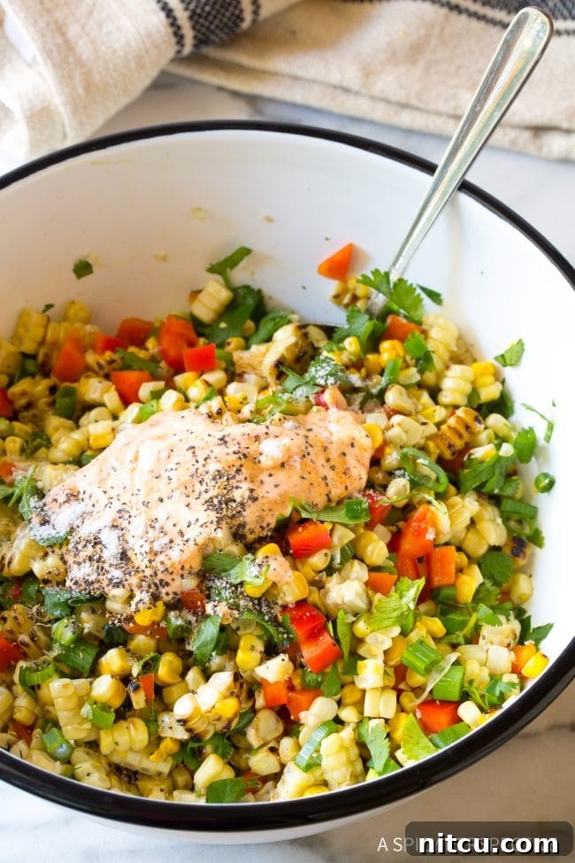 Charred Mexican Elote 9 Creamy salad dressing being gracefully tossed into the colorful street corn salad ingredients, ensuring even coating.
