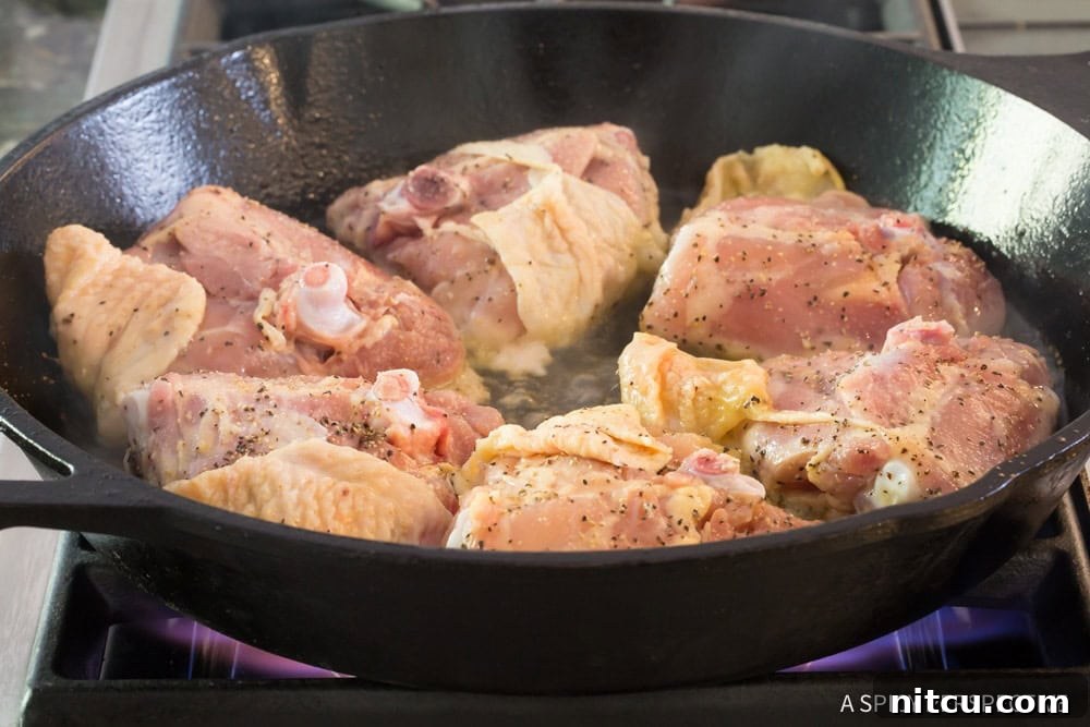 Chicken thighs cooking in a cast iron skillet skin-side down, showcasing the sizzling oil and browning skin.