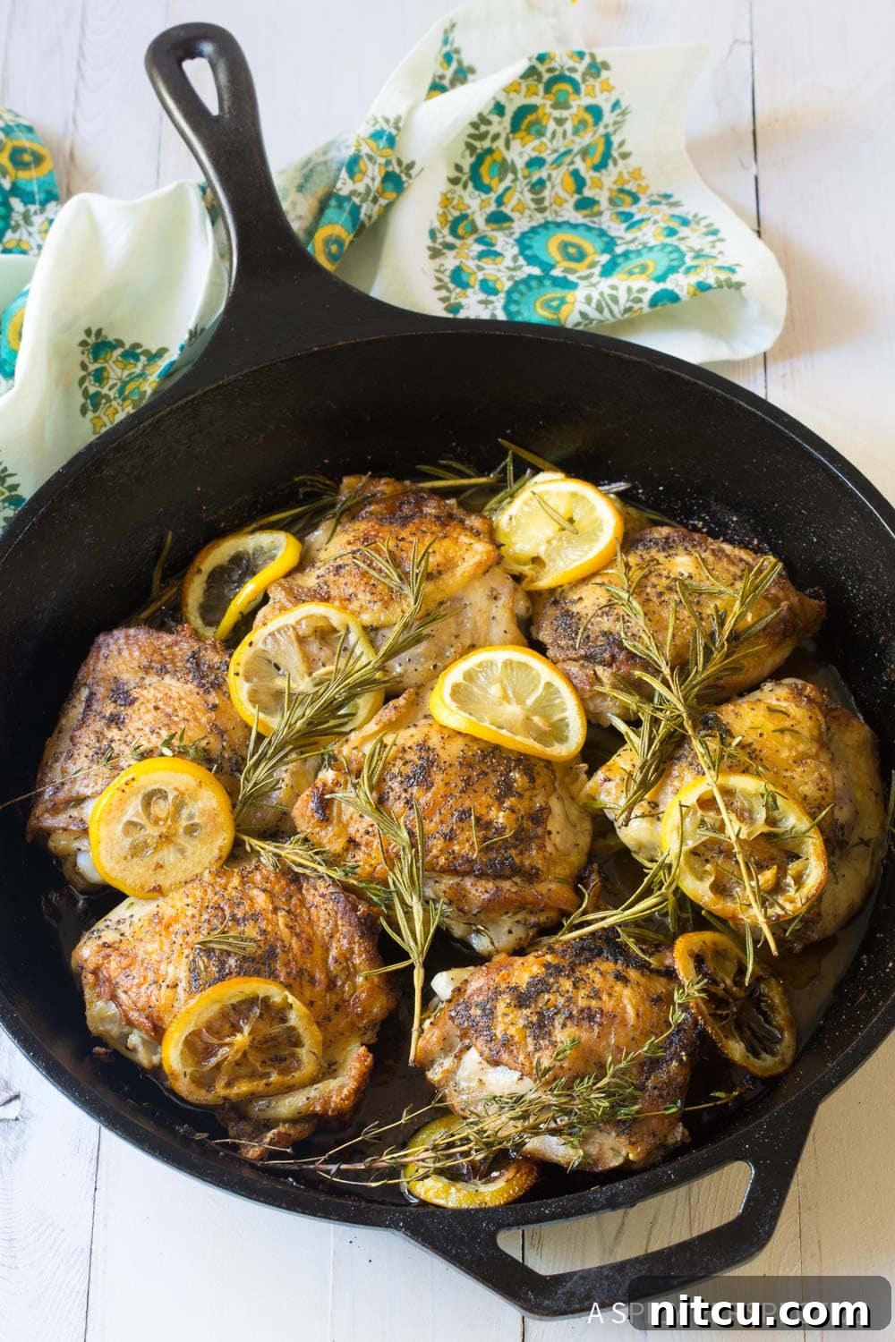 Perfectly cooked chicken thighs with a vibrant display of fresh herbs and lemon in a cast iron skillet, ready for serving.