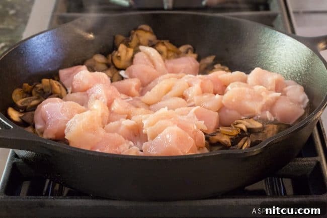 Lighter Chicken A La King 7 Cubed raw chicken breast added to sauteed mushrooms and onions in a skillet.
