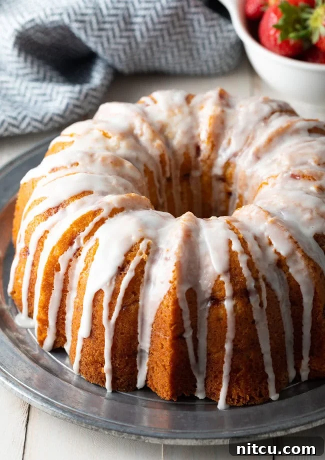 Strawberry Bliss Bundt 11 A fully prepared and beautifully glazed strawberry bundt cake, garnished with fresh berries, sitting on a silver serving plate, inviting guests to indulge.