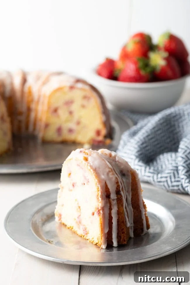 Strawberry Bliss Bundt 12 A delectable slice of strawberry lemon bundt cake on a silver plate, showing off its tender crumb and rich strawberry distribution.