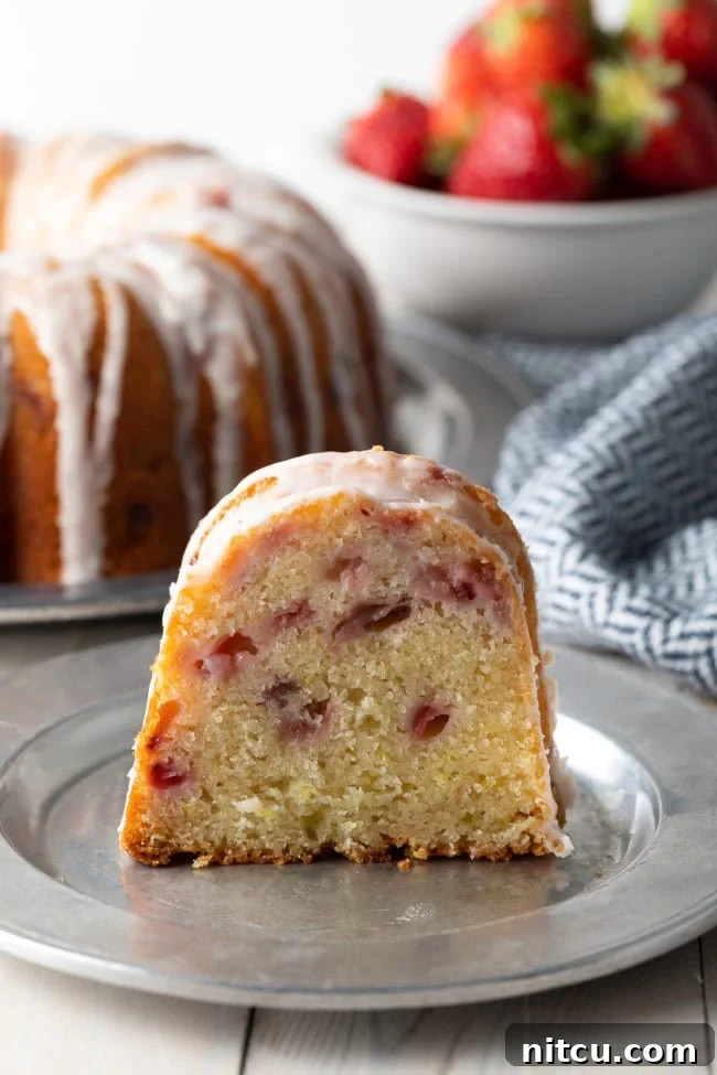 Strawberry Bliss Bundt 3 A perfect slice of the Strawberry Bundt Cake, showcasing its moist interior, studded with fresh strawberries, and topped with a luscious lemon glaze. The slice sits on a silver plate, ready to be enjoyed.