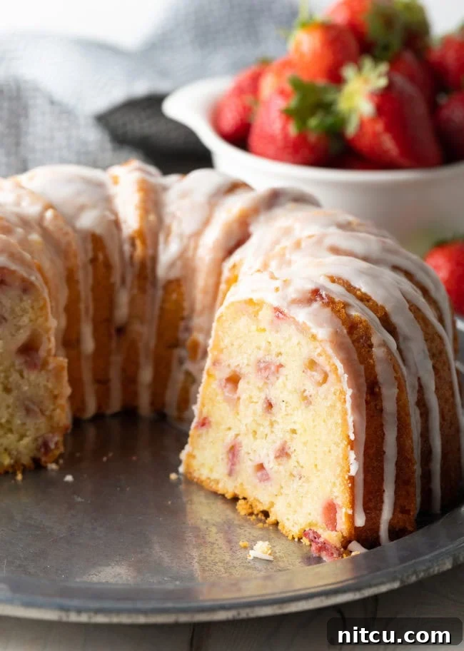 Strawberry Bliss Bundt 4 A freshly baked Strawberry Bundt Cake with a slice removed, revealing the soft, moist interior dotted with cooked strawberries. The cake is lightly glazed and sitting on a wire rack to cool.