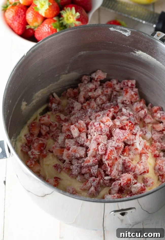 Strawberry Bliss Bundt 7 Strawberry bundt cake batter in a mixing bowl with fresh chopped strawberries placed on top, ready to be folded in.