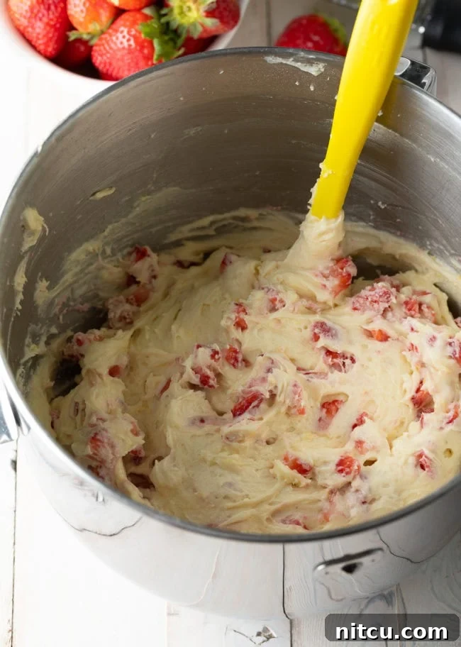 Strawberry Bliss Bundt 8 Strawberry cake batter with strawberries added and being gently stirred with a yellow spatula, ensuring even distribution.
