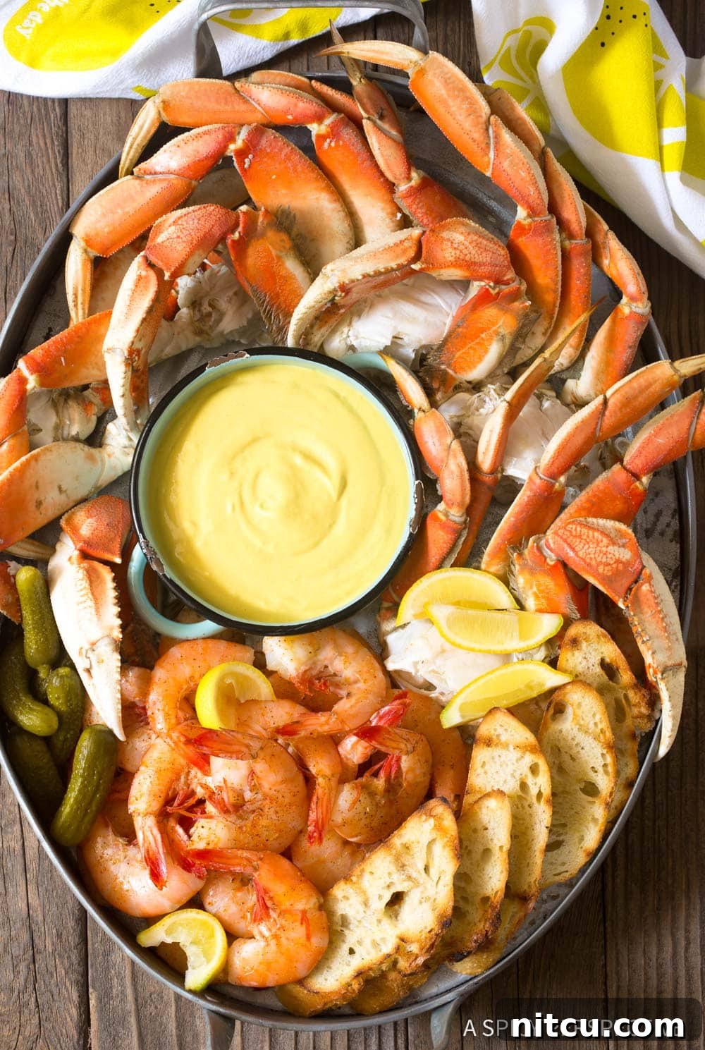 Spicy-Mustard-Seafood-Sauce A bowl of vibrant yellow Spicy Mustard Seafood Sauce on a wooden board next to fresh crab legs and lemon wedges.