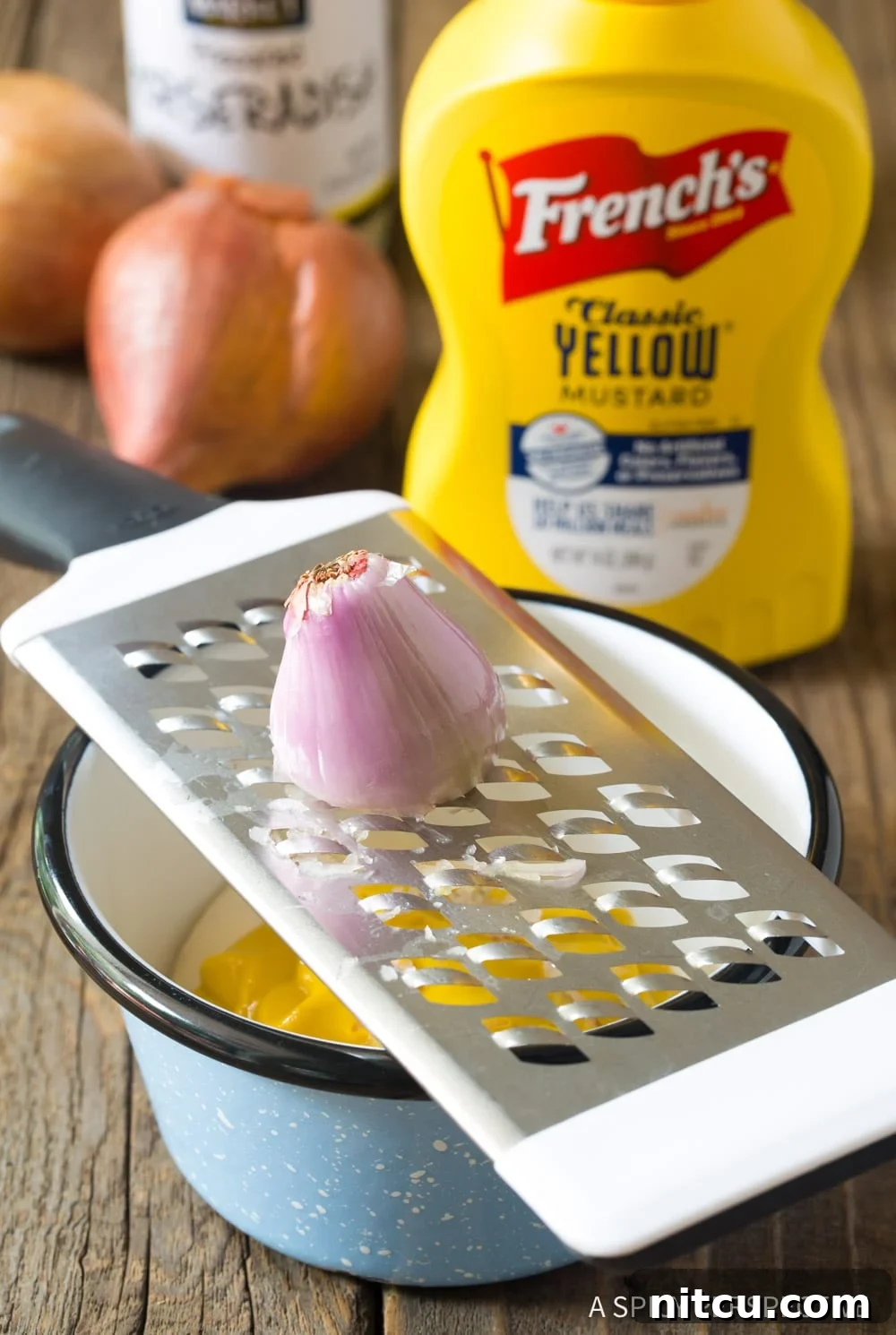 Spicy-Mustard-Sauce A hand grating a shallot directly into a bowl of the mustard sauce mixture, ensuring fine pieces.