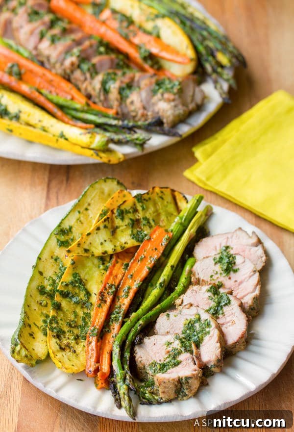 Flame-Kissed Pork Tenderloin with Bright Chimichurri and Rustic Roast Vegetables 2 Sliced grilled pork tenderloin with chimichurri and roasted vegetables on a plate, garnished with fresh herbs, ready to be served.