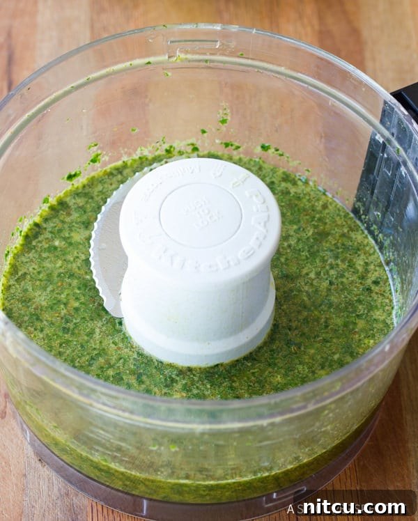 Flame-Kissed Pork Tenderloin with Bright Chimichurri and Rustic Roast Vegetables 4 Fresh chimichurri sauce being prepared in a food processor, showing a vibrant green mixture of fresh herbs, garlic, and olive oil actively blending.