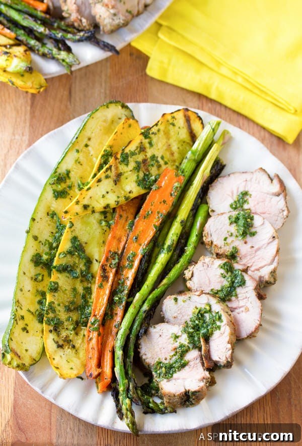 Flame-Kissed Pork Tenderloin with Bright Chimichurri and Rustic Roast Vegetables 10 A close-up of perfectly grilled pork tenderloin slices, generously topped with fresh, vibrant green chimichurri sauce on a white plate, ready to be enjoyed.