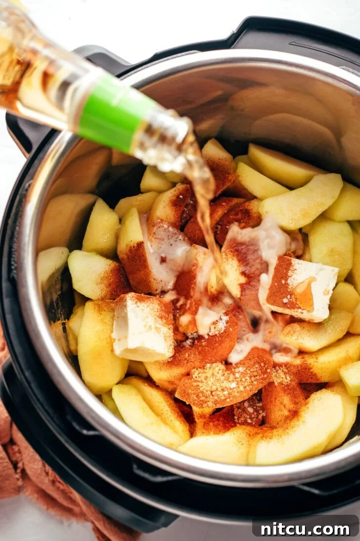 fast-side-dish Ingredients for spiced apples in a pressure cooker while cider is being poured into the mix.