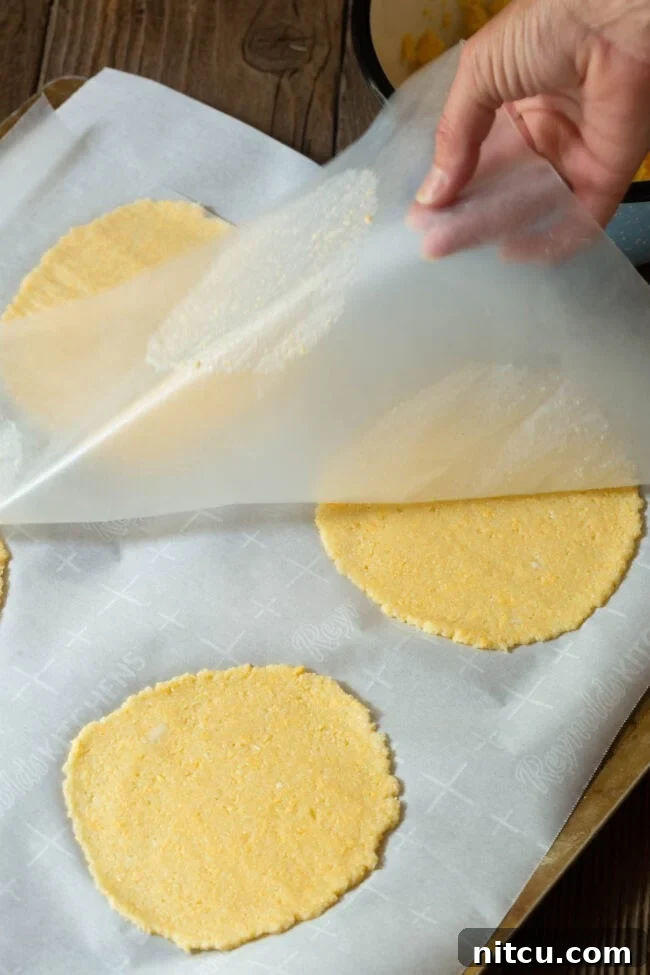 low-carb Hand pulling back the top layer of parchment to reveal perfectly flat, baked tortillas.