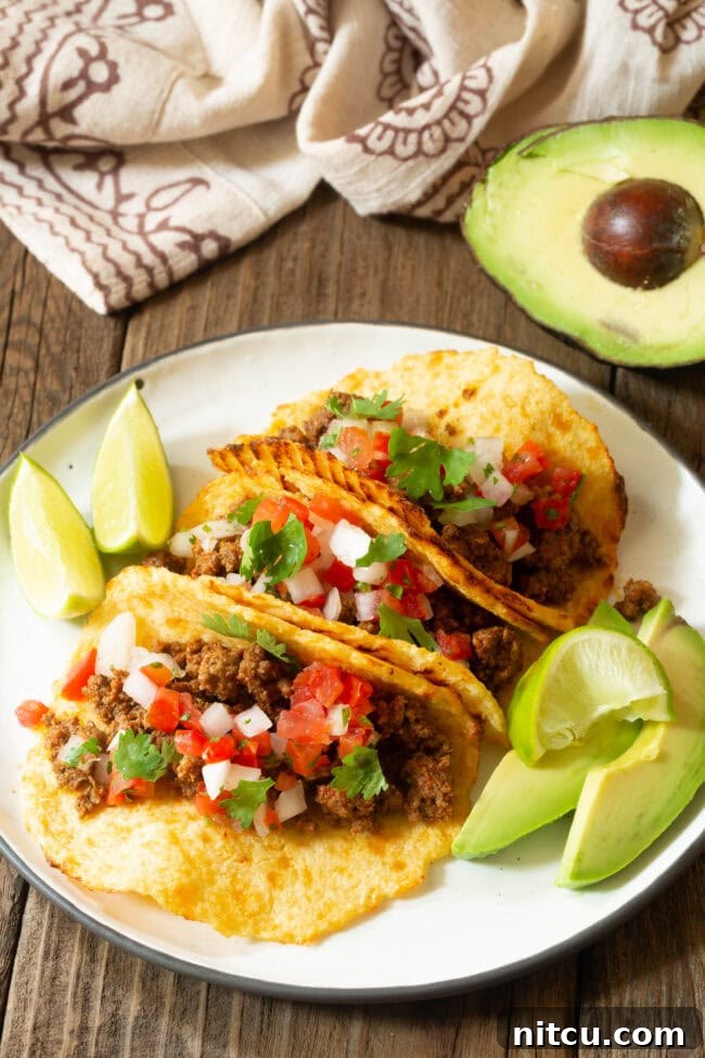 tortilla-carbs Three perfectly assembled tacos on a plate with lime wedges and avocado slices on the side.