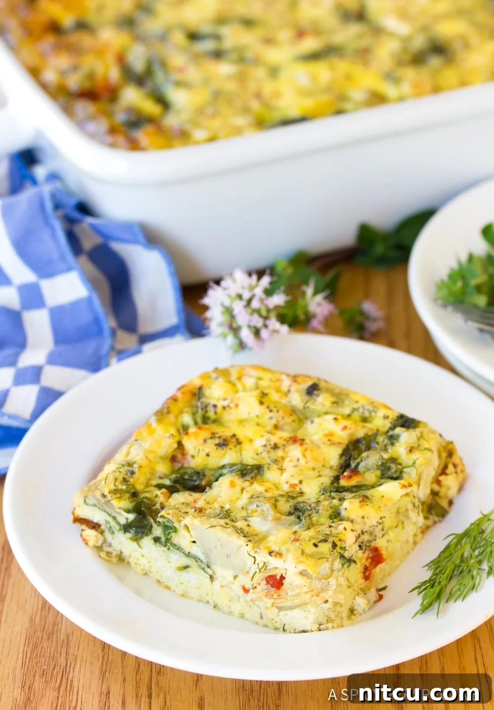 Savory Greek Omelette Bake 2 A close up photo of a slice of Greek omelette casserole on a white plate, showcasing its vibrant ingredients and fluffy texture.