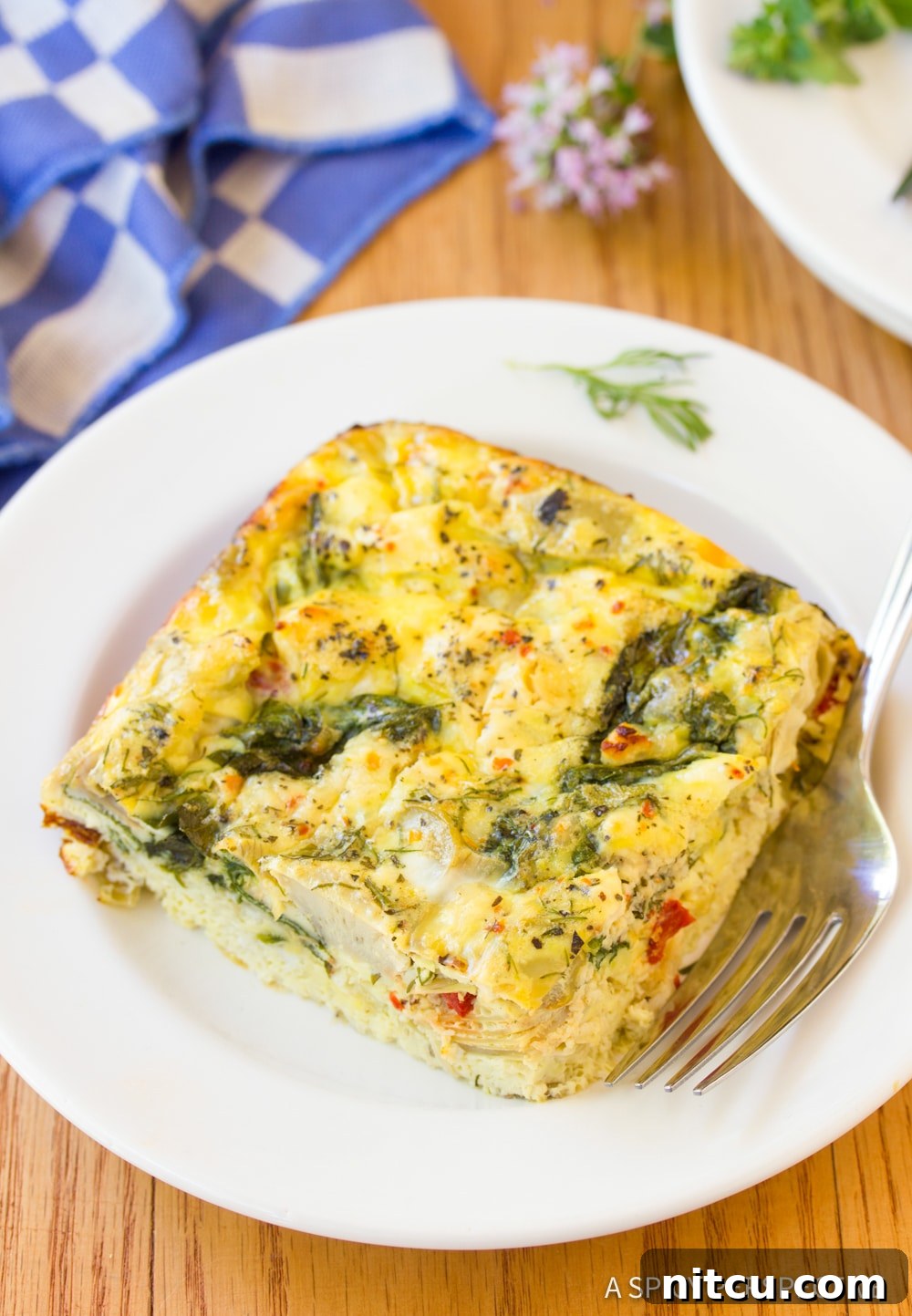 Savory Greek Omelette Bake 3 A beautifully presented slice of Greek omelette casserole on a white plate, garnished with fresh herbs, ready to be enjoyed.