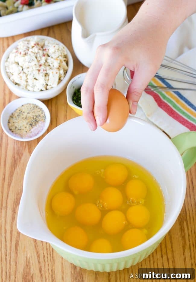 Savory Greek Omelette Bake 6 A close-up of a hand cracking a fresh egg into a white mixing bowl, ready for whisking.