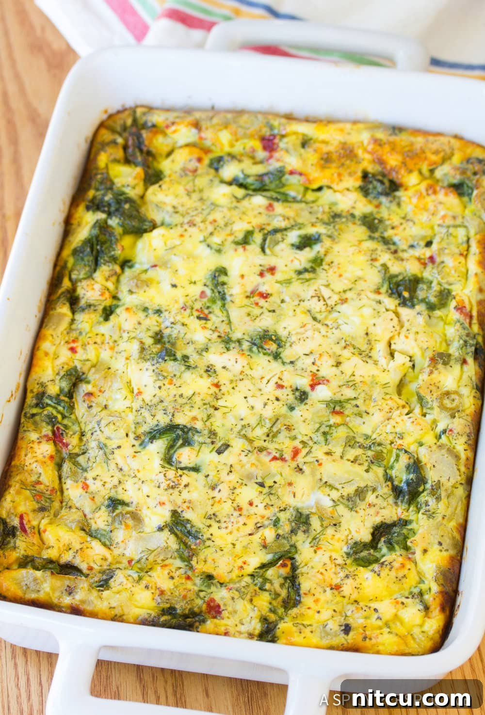 Savory Greek Omelette Bake 8 A close up view of a golden-brown Greek omelette casserole in a white baking dish, ready to be portioned and served.