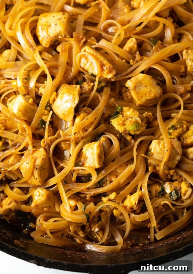 Classic Chicken Pad Thai Stir-fry 11 Close-up, top-down view of authentic Pad Thai chicken with noodles in a cast iron skillet, highlighting the rich texture and garnishes.