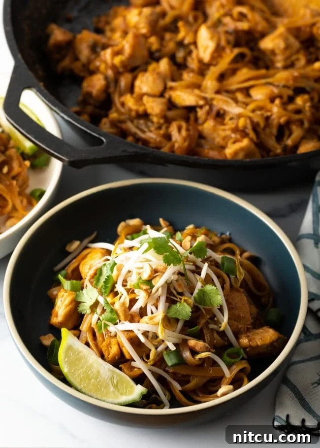 Classic Chicken Pad Thai Stir-fry 12 Homemade Pad Thai noodles in a bowl, exquisitely garnished with fresh mung bean sprouts, bright lime wedges, and fragrant cilantro, ready for a delicious meal.
