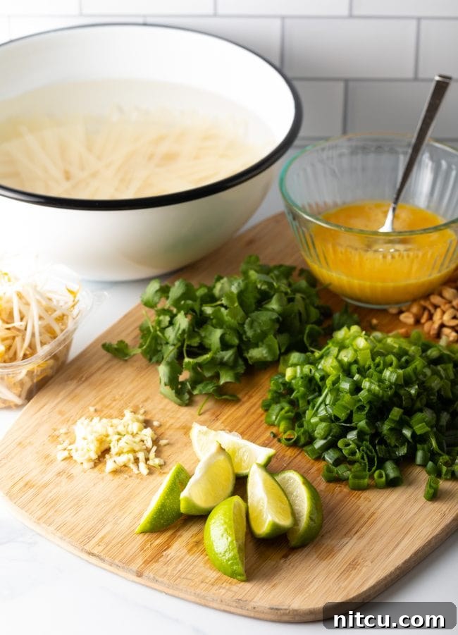 Classic Chicken Pad Thai Stir-fry 4 A wooden cutting board displaying neatly arranged Pad Thai ingredients: minced garlic, fresh lime wedges, chopped green onions, cilantro, and a bowl of beaten eggs.
