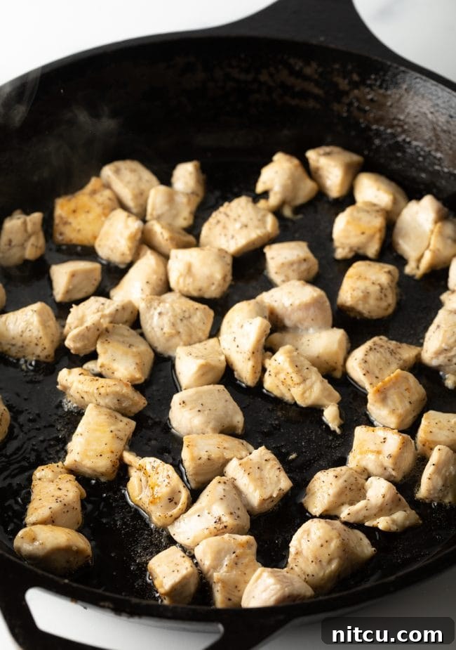 Classic Chicken Pad Thai Stir-fry 6 Bite-sized chicken pieces sizzling and cooking in a large, hot skillet, forming the base of the stir-fry.