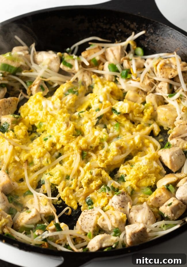 Classic Chicken Pad Thai Stir-fry 8 Scrambled eggs being incorporated into the stir-fry with chicken, bean sprouts, green onions, and garlic in a large skillet.