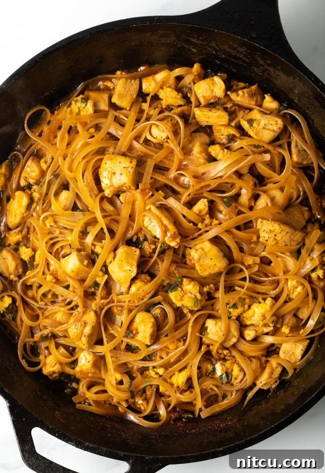 Classic Chicken Pad Thai Stir-fry 10 Top-down view of authentic Pad Thai chicken with noodles, served hot in a cast iron skillet.