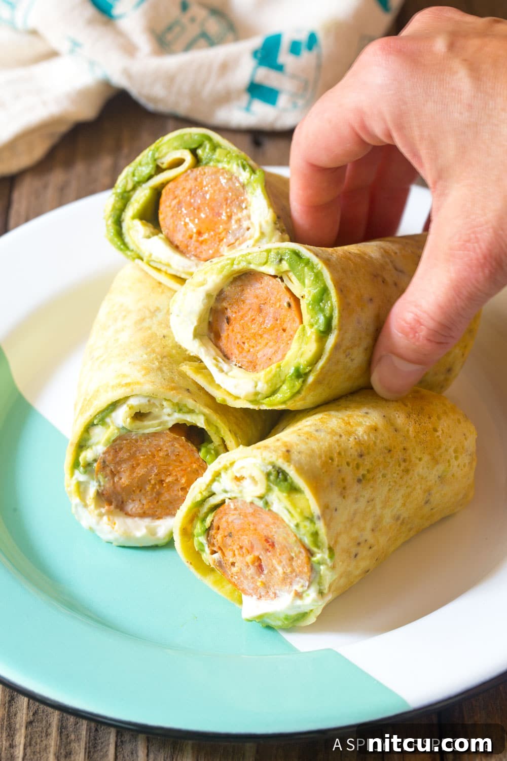 Quick Keto Egg Wraps 2 Breakfast egg wraps on a plate with a hand grabbing one.