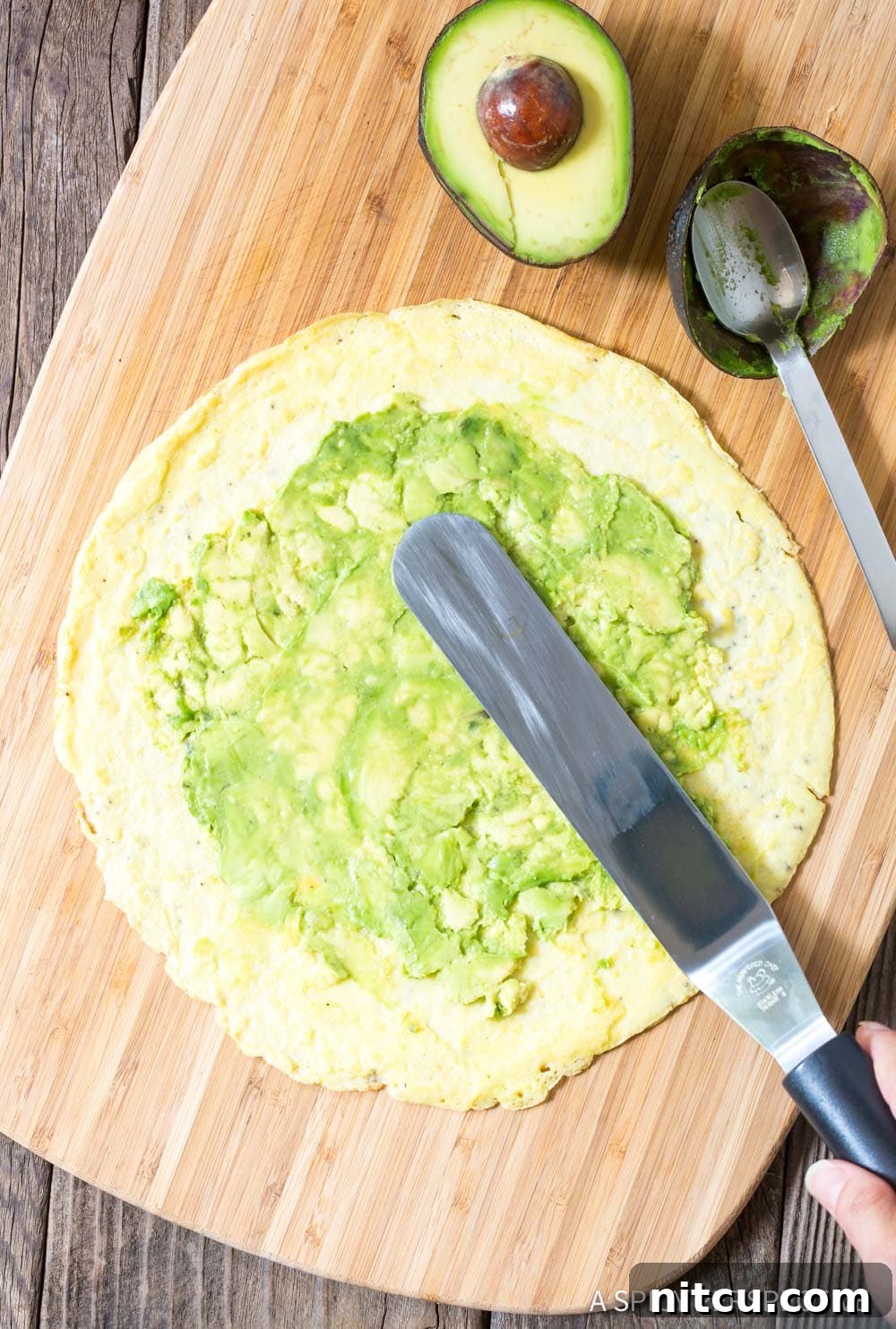 Quick Keto Egg Wraps 6 Hand spreading smashed avocado over an egg wrap.