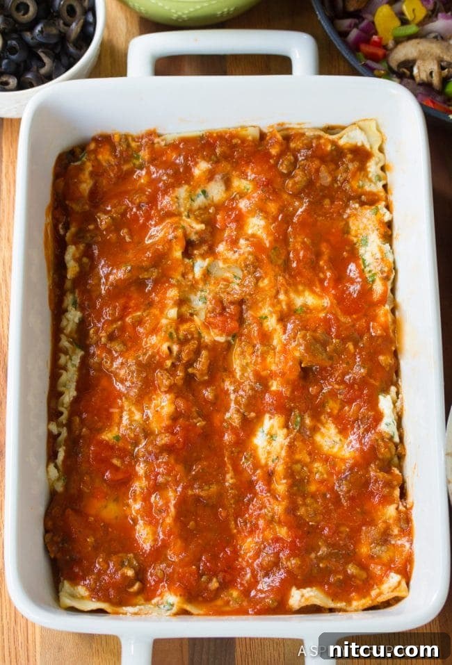 Fully Loaded Pizza Lasagna 5 An overhead view of the Supreme Pizza Lasagna being carefully layered in a white baking dish, showing the organized placement of noodles, cheese, sauce, and vegetables.