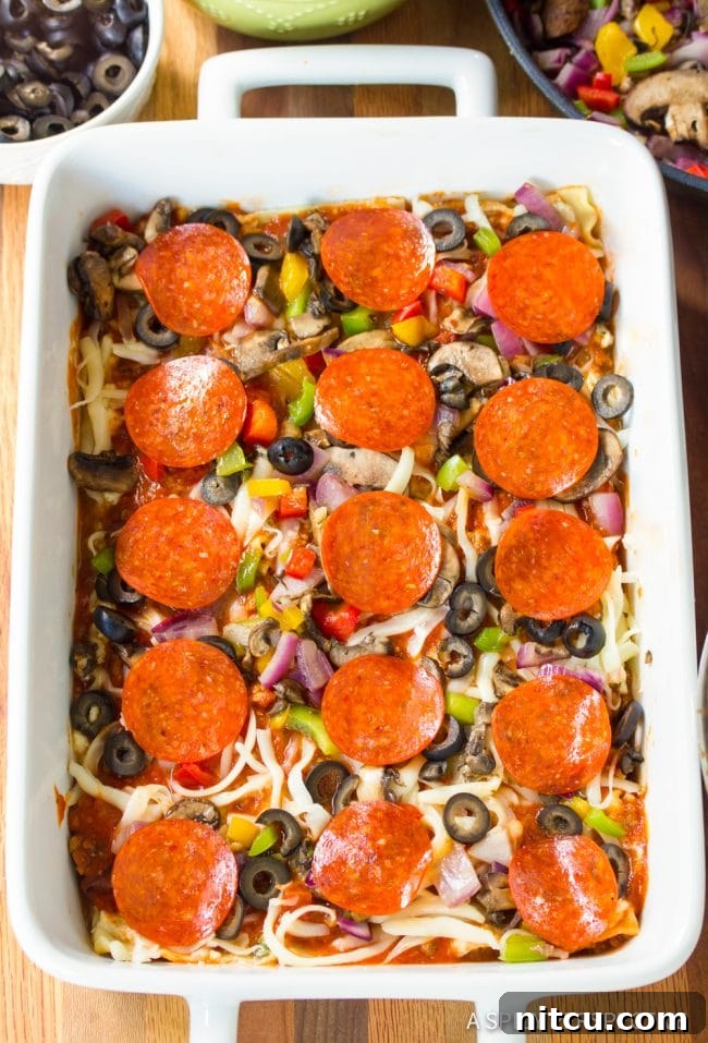 Fully Loaded Pizza Lasagna 6 A second overhead view of the Supreme Pizza Lasagna mid-layering in a white pan, showcasing the vibrant ingredients and building structure before baking.