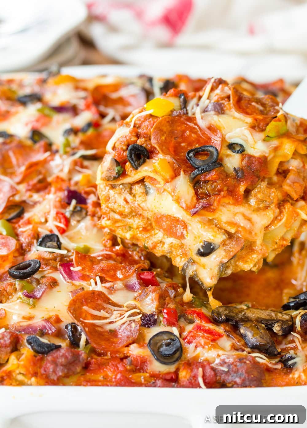Fully Loaded Pizza Lasagna 8 A knife gently slicing into a pan of freshly baked Supreme Pizza Lasagna, revealing the luscious, cheesy layers within.