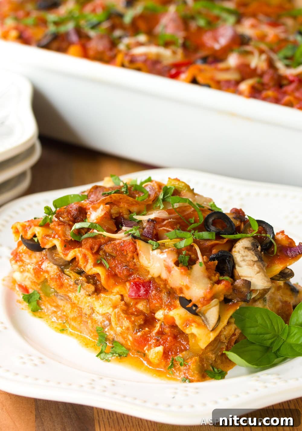 Fully Loaded Pizza Lasagna 9 A tempting, golden-brown slice of Supreme Pizza Lasagna, generously topped with melted cheese and pepperoni, beckons from a white plate.