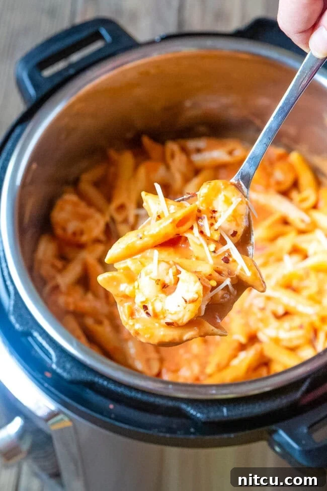 Velvety Instant Pot Vodka Shrimp Pasta 3 Shrimp pasta in an instant pot with a spoon hovering over it with a bite of pasta.